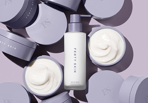 Product shot of Butta Drop Body Milk in the middle of multiple open Butta Drop Whipped Oil Body Cream on a lavender background. Product shot of Butta Drop Body Milk in the middle of multiple open Butta Drop Whipped Oil Body Cream on a lavender background.